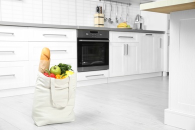 Photo of Textile shopping bag full of vegetables and baguette on floor in kitchen. Space for text