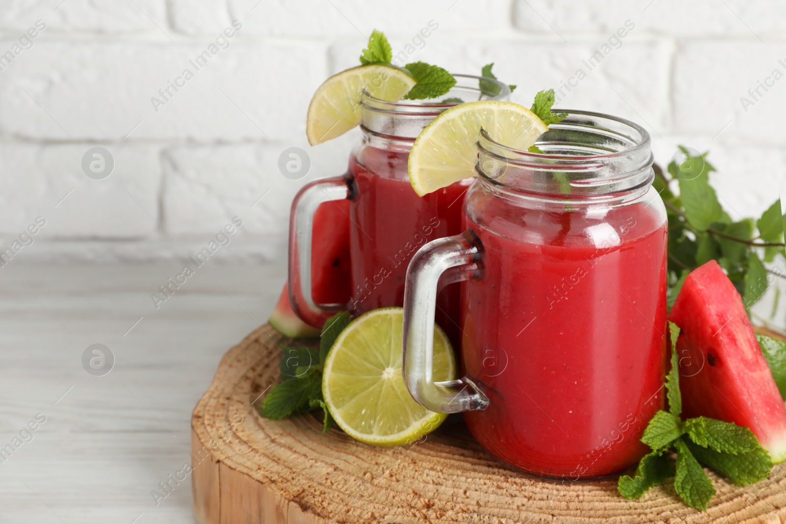 Photo of Tasty summer watermelon drink, limes and mint on white wooden table, space for text