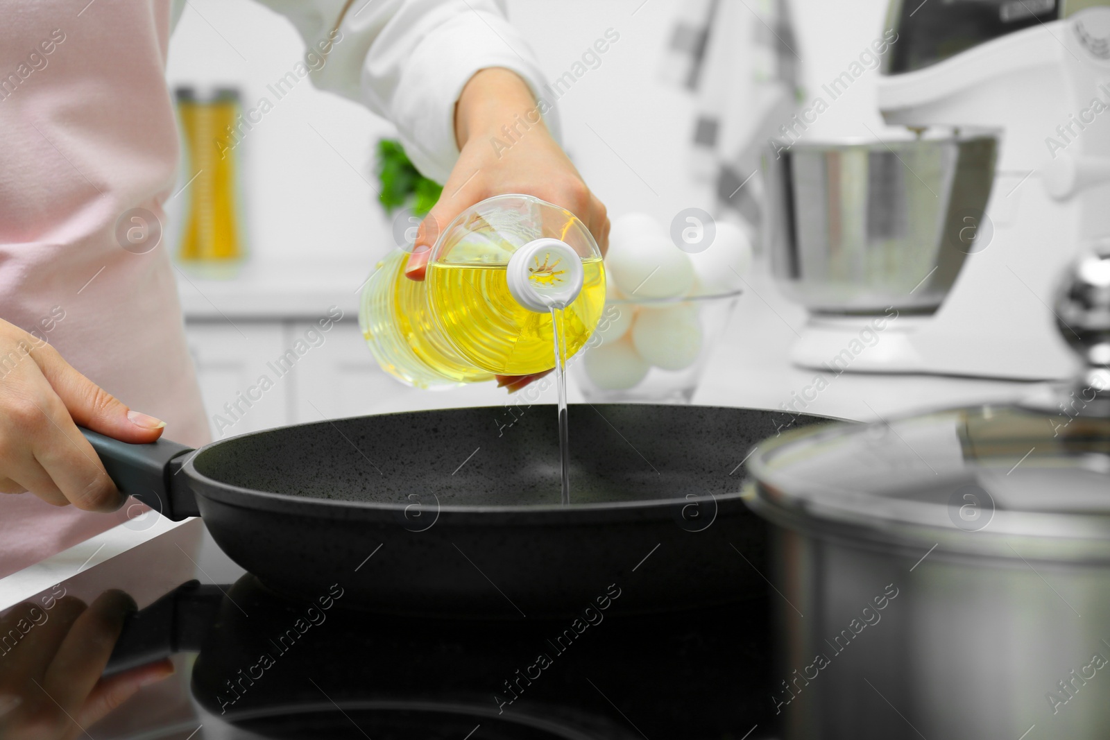 Photo of Woman pouring cooking oil from bottle into frying pan in kitchen, closeup