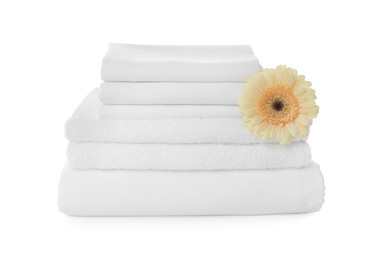 Stack of towels and bed sheets with gerbera on white background