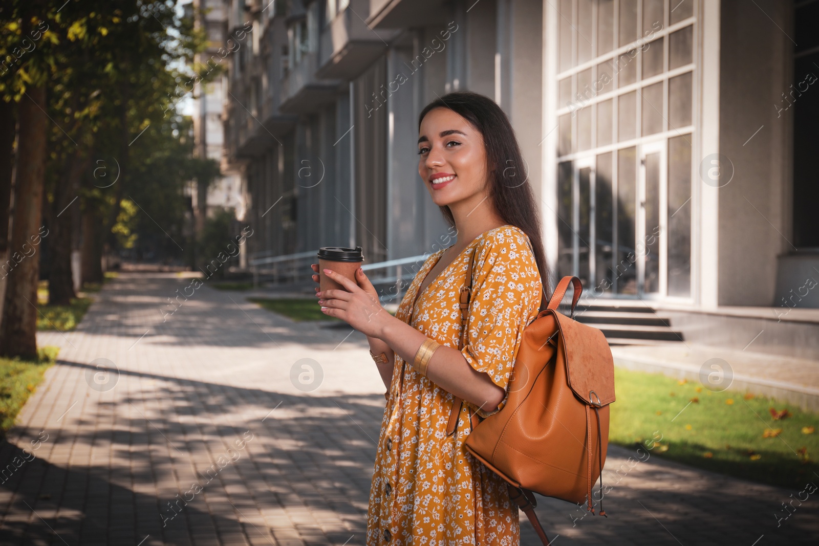 Photo of Beautiful young woman with stylish backpack and cup of coffee on city street