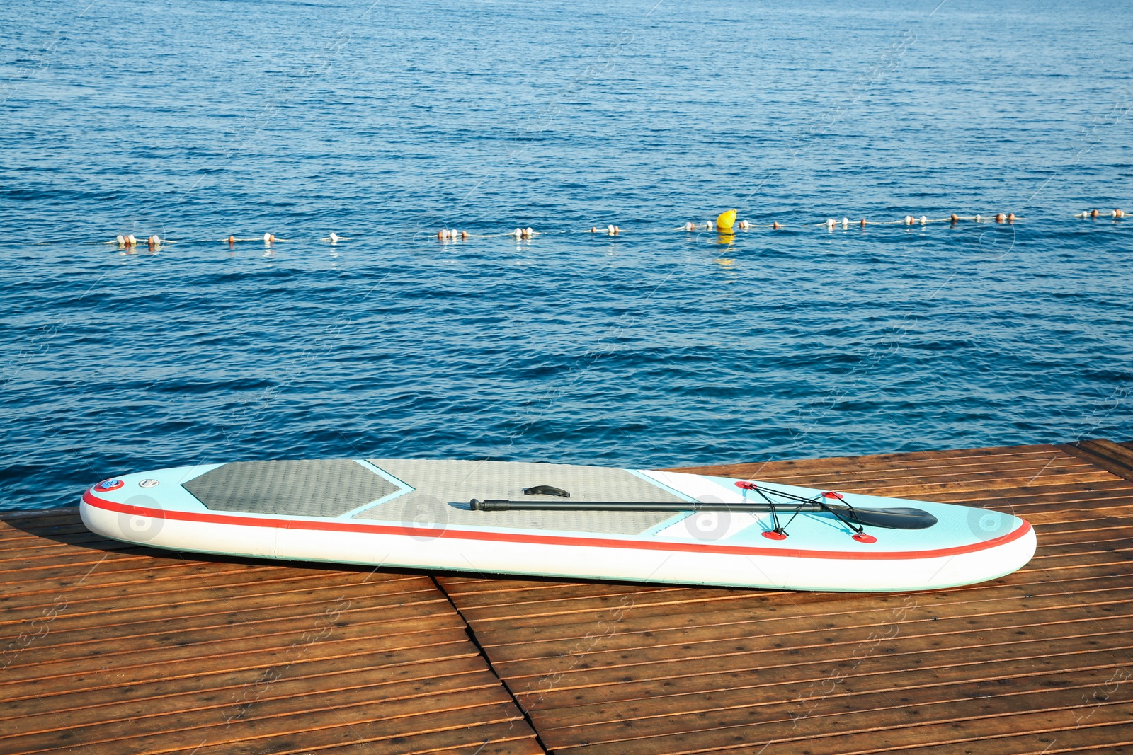 Photo of SUP board with paddle on wooden pier near sea