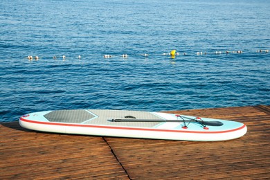 SUP board with paddle on wooden pier near sea