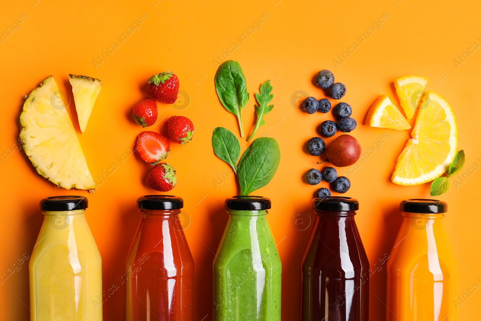 Photo of Flat lay composition with bottles of delicious juices and fresh ingredients on orange background