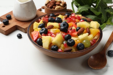 Photo of Delicious fruit salad in bowl, berries, fresh mint and nuts on white marble table