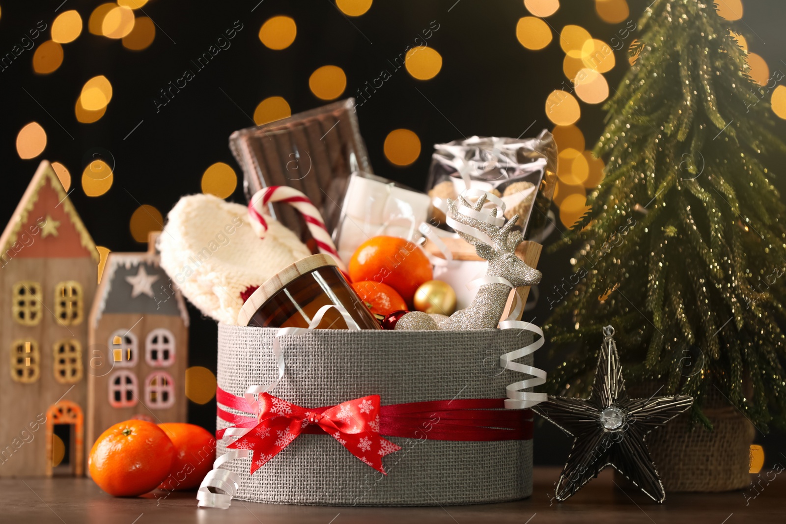 Photo of Basket with Christmas gift set and small fir tree on wooden table against blurred festive lights