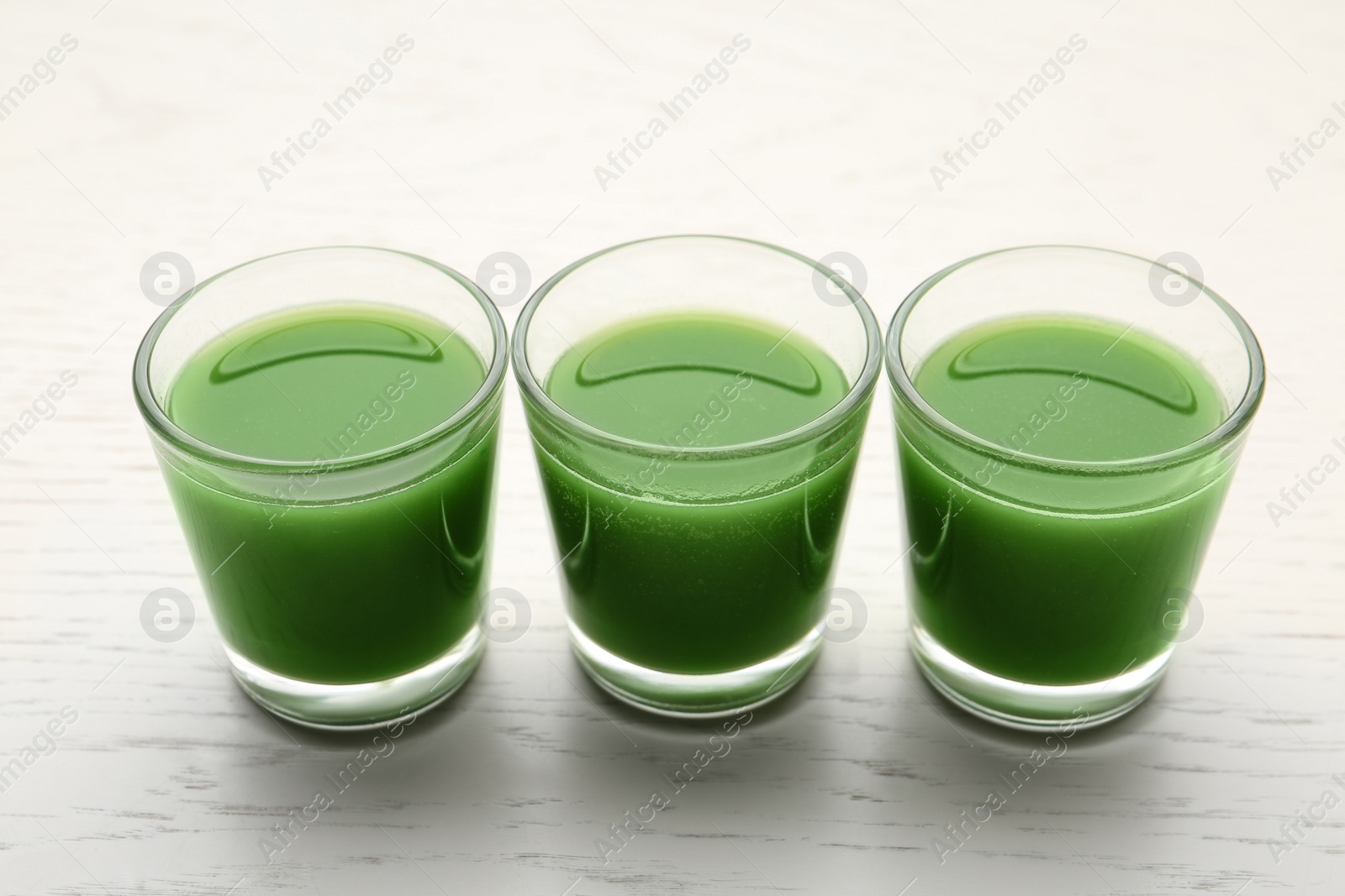 Fresh wheat grass juice in glasses on white wooden background Photo of Fresh wheat grass juice in glasses on white wooden background