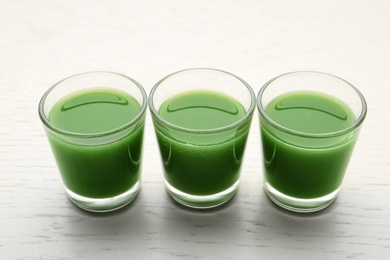 Photo of Fresh wheat grass juice in glasses on white wooden background