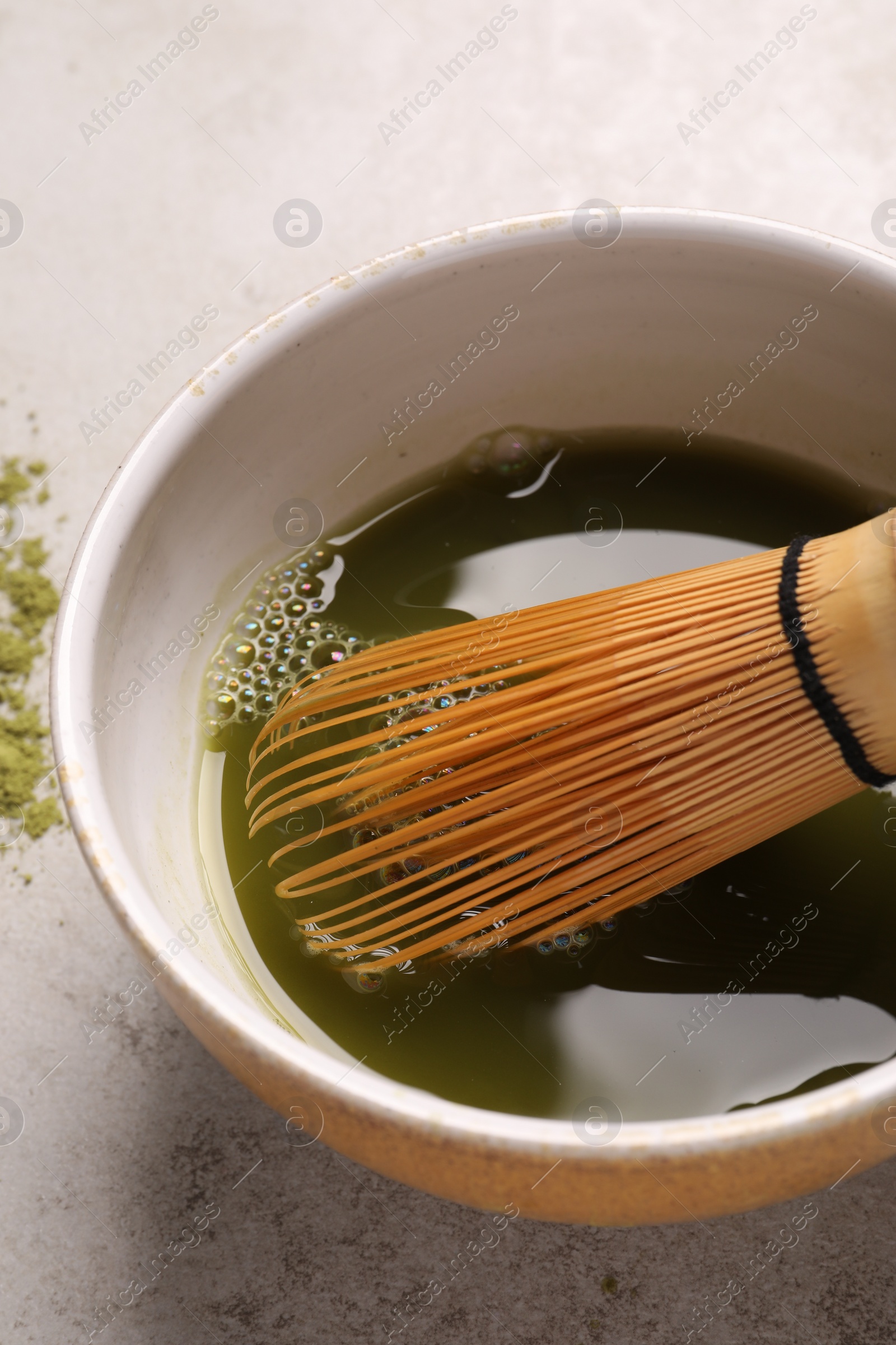 Photo of Bowl of fresh matcha tea with bamboo whisk on light table