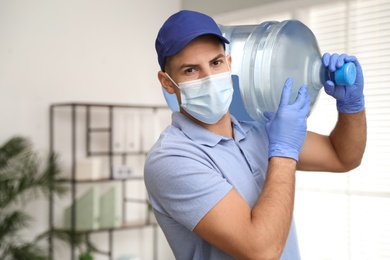 Photo of Courier in face mask with bottle of cooler water indoors, space for text. Delivery during coronavirus quarantine
