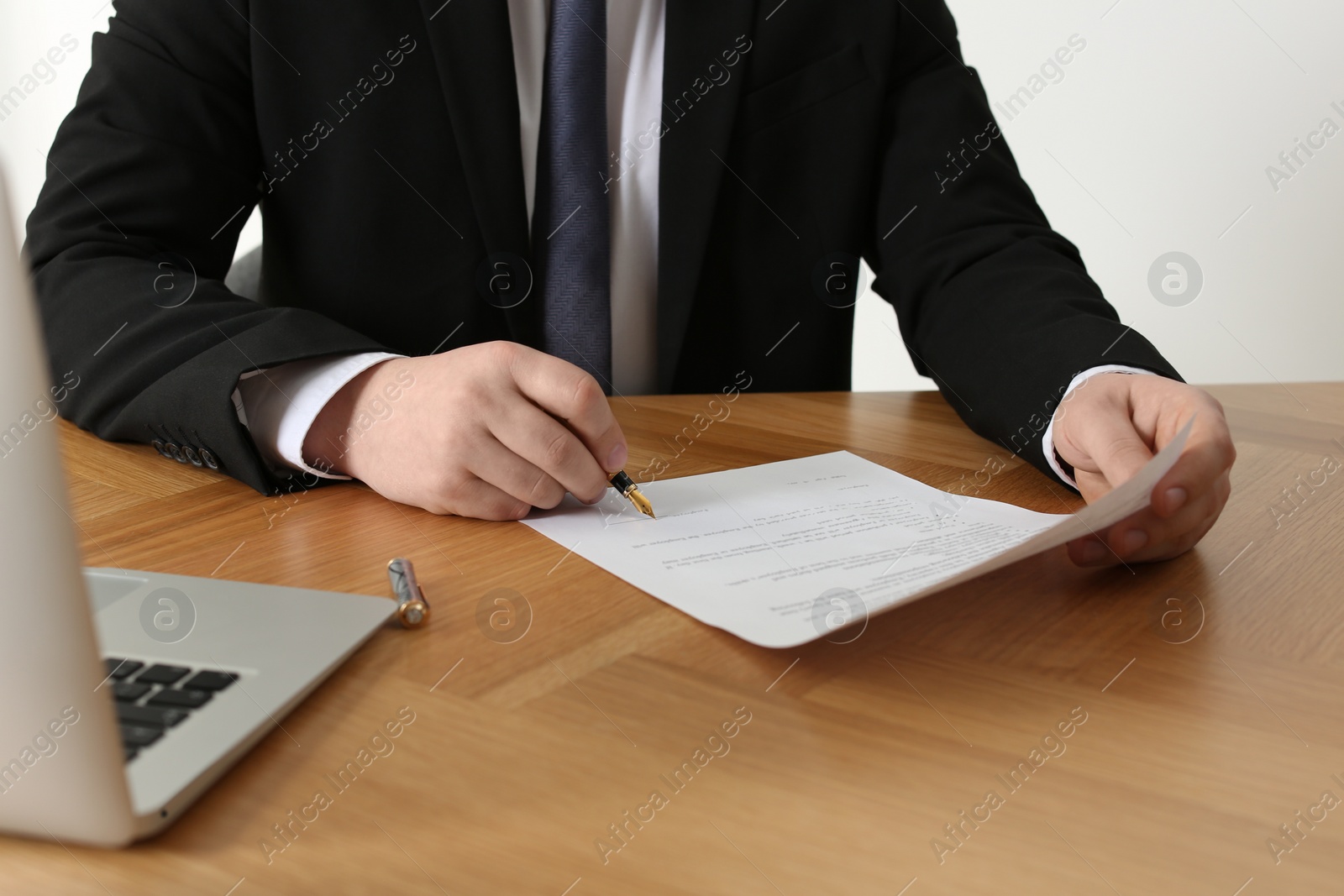 Photo of Notary signing document at wooden table, closeup