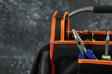 Photo of Bag with needle nose pliers, screwdriver and other repair tools on dark background, closeup. Space for text