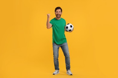 Emotional sports fan with soccer ball on orange background