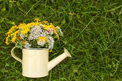 Photo of Pale yellow watering can with beautiful flowers on green grass, top view. Space for text