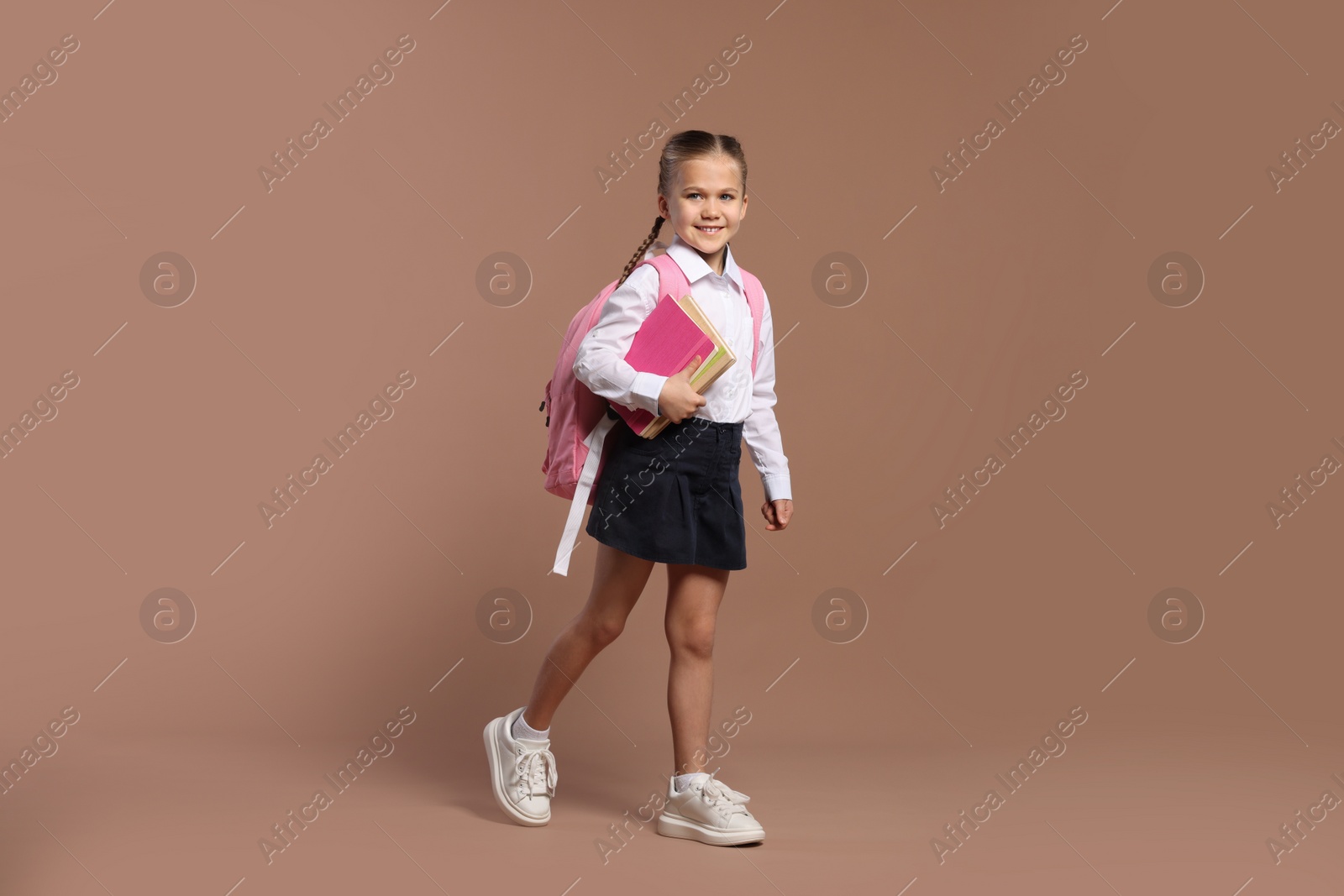 Photo of Happy schoolgirl with backpack and books on brown background