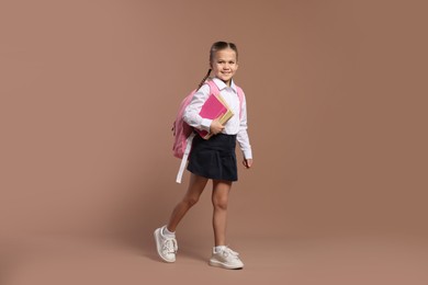 Happy schoolgirl with backpack and books on brown background