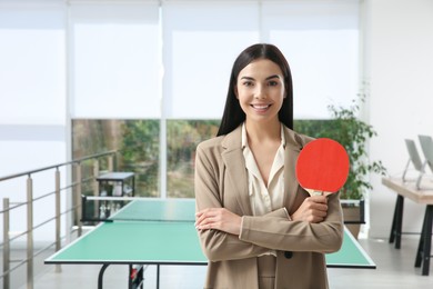 Business woman with tennis racket near ping pong table in office. Space for text