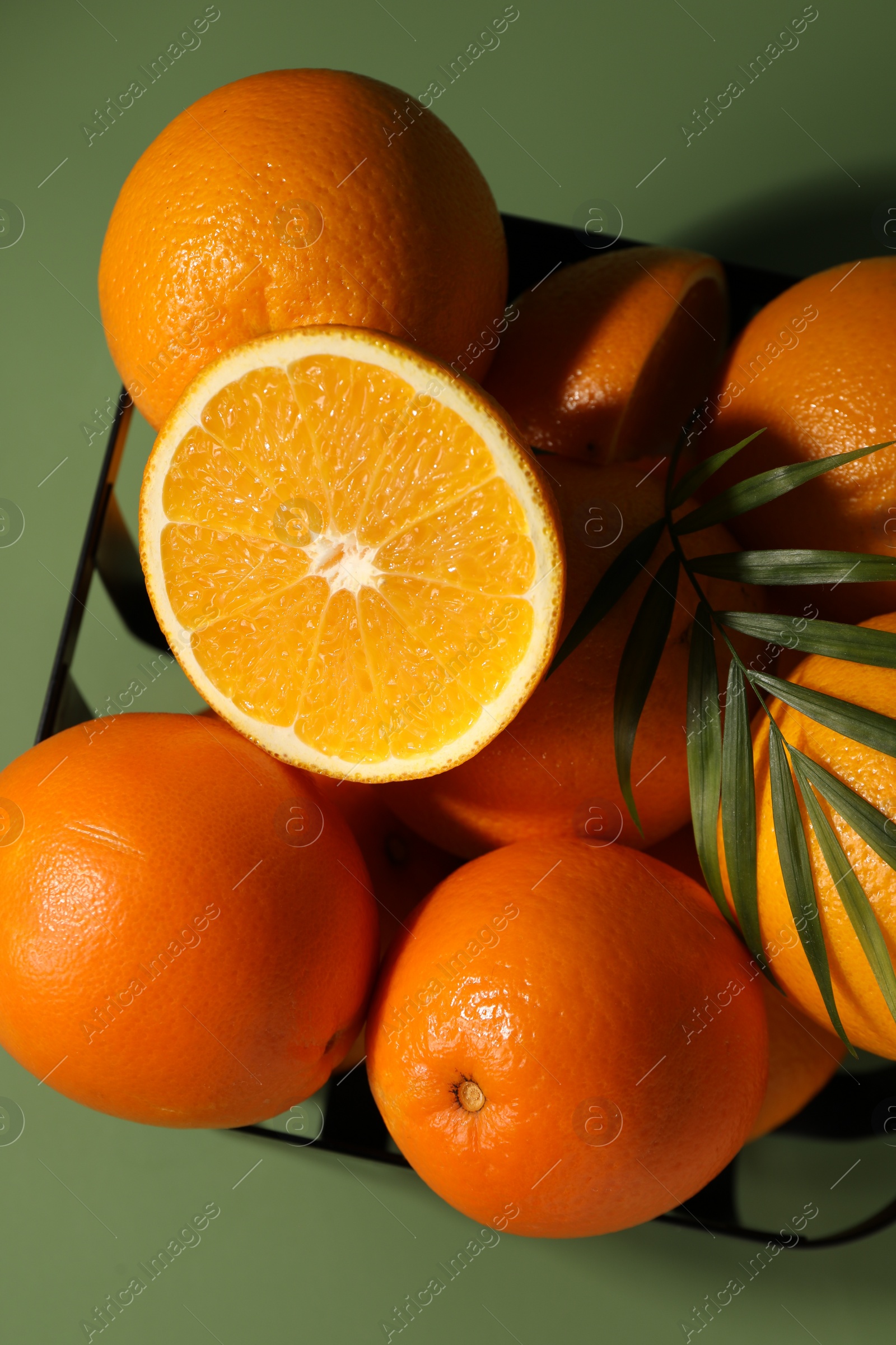 Photo of Fresh oranges in metal basket on green background, top view