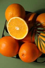 Fresh oranges in metal basket on green background, top view