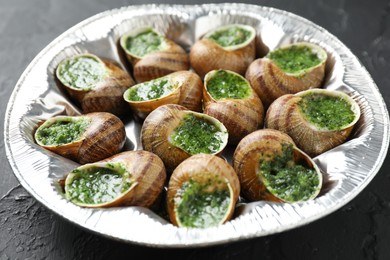 Photo of Delicious cooked snails on dark textured table, closeup