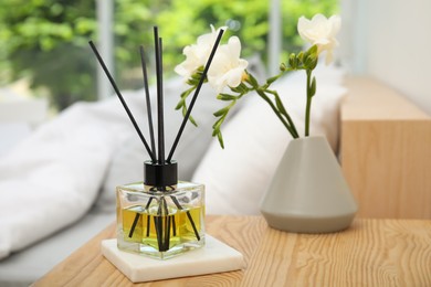 Reed diffuser and vase with bouquet on wooden nightstand in bedroom