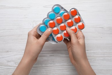 Woman holding blisters with cough drops on white wooden background, top view