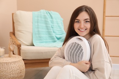 Photo of Happy young woman with modern electric fan heater at home