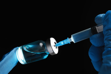 Doctor filling syringe with medication on black background, closeup. Vaccination and immunization