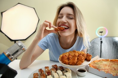 Photo of Food blogger eating in front of microphone at table against light background. Mukbang vlog
