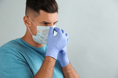 Photo of Man in medical gloves putting on protective face mask against grey background. Space for text