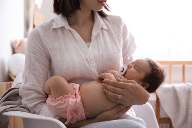 Mother holding her cute little baby with pacifier at home, closeup