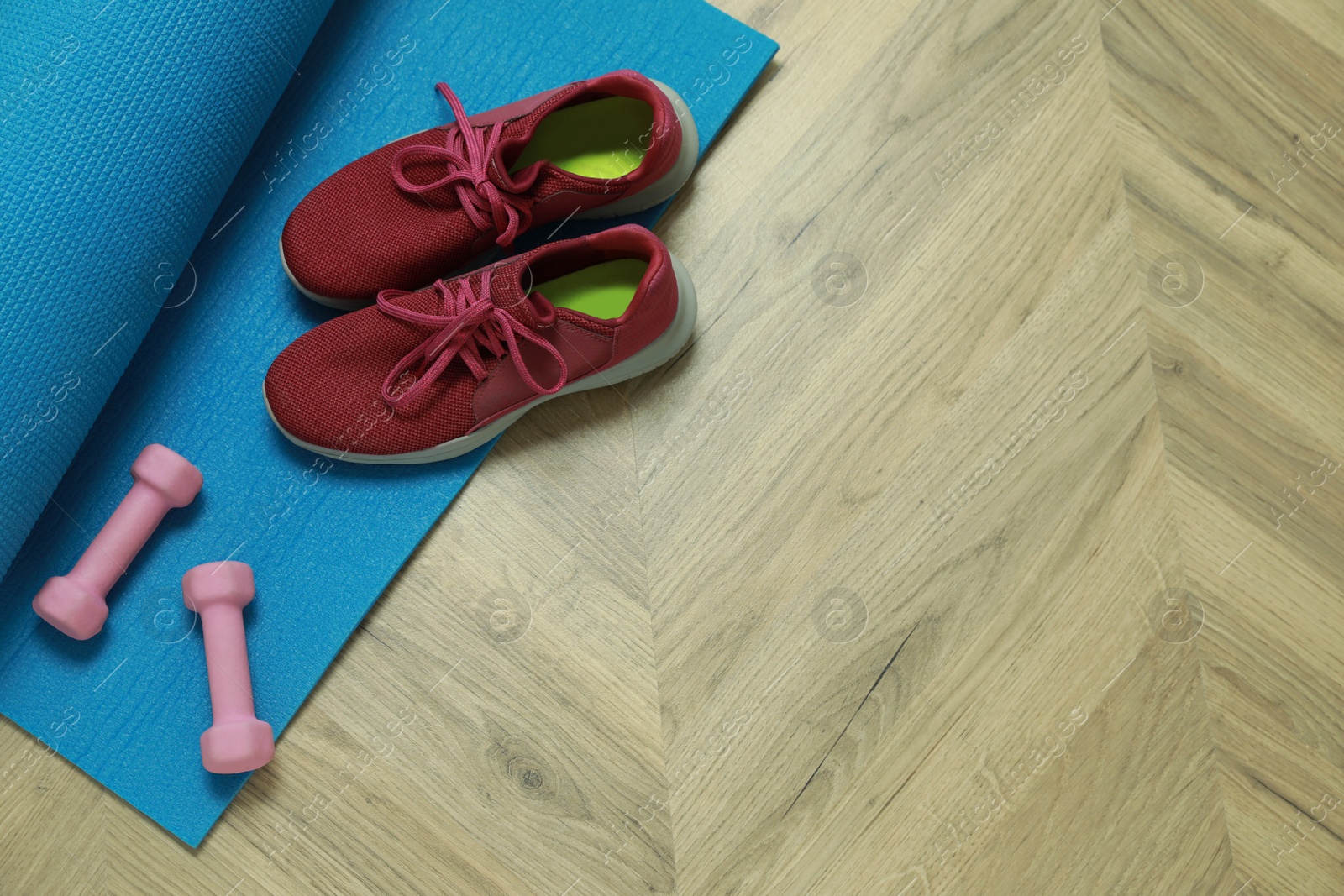 Photo of Dumbbells, sneakers and mat on wooden floor, above view. Space for text