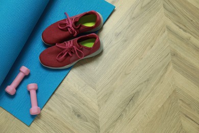 Photo of Dumbbells, sneakers and mat on wooden floor, above view. Space for text