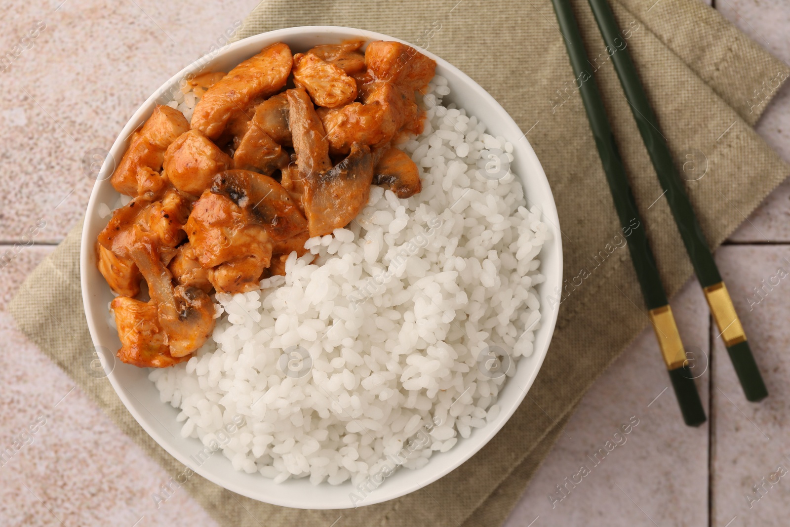 Photo of Bowl of delicious rice with meat, mushrooms and chopsticks on tiled table, flat lay