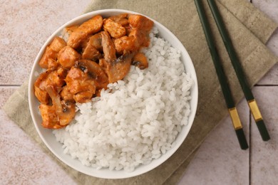 Photo of Bowl of delicious rice with meat, mushrooms and chopsticks on tiled table, flat lay