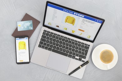 Photo of Online store website on laptop screen. Computer, smartphone, stationery, credit card and coffee on grey table, flat lay