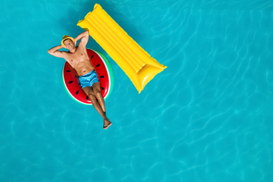 Image of Happy man with inflatable mattress and ring in swimming pool, top view. Summer vacation