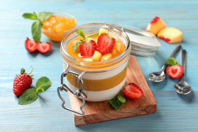 Photo of Delicious panna cotta with mango coulis and fresh fruit pieces on light blue wooden table