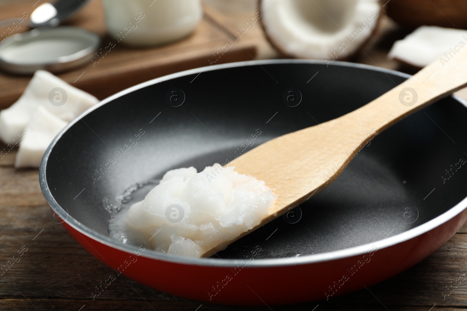 Photo of Frying pan with coconut oil and wooden spatula on wooden table. Healthy cooking