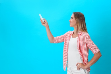 Photo of Young woman with air conditioner remote on blue background. Space for text
