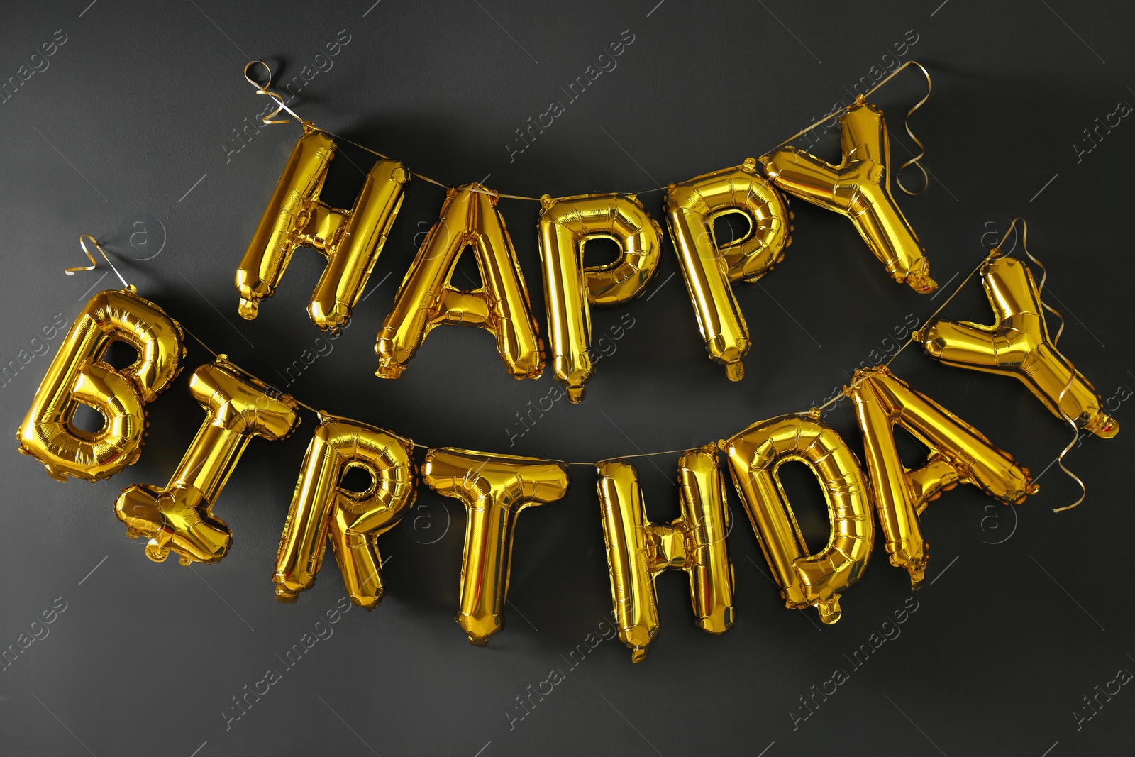 Photo of Phrase HAPPY BIRTHDAY made of golden balloon letters on black wall