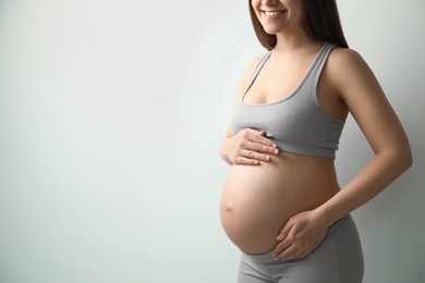 Pregnant young woman touching belly on light background, closeup. Space for text