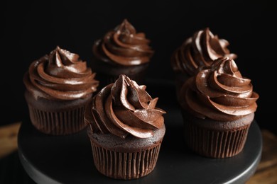 Delicious chocolate cupcakes with cream on dessert stand against black background, closeup