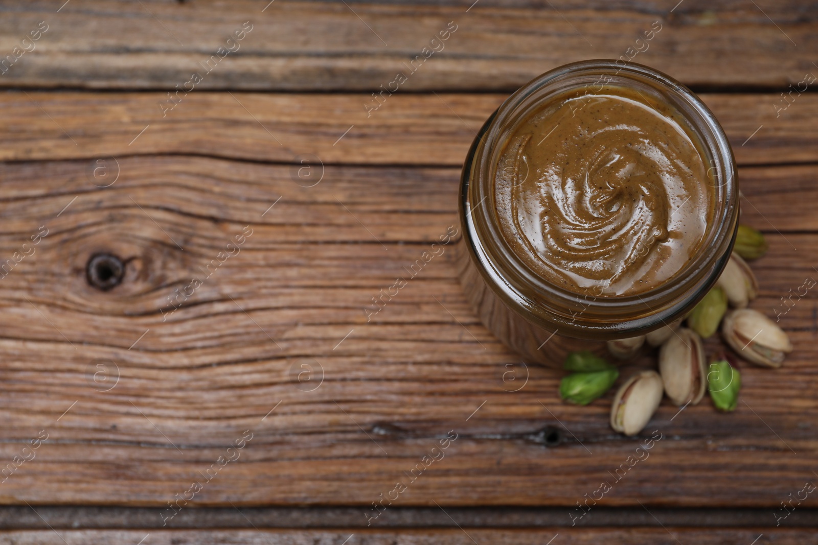 Photo of Tasty pistachio nut paste in jar on wooden table, top view. Space for text