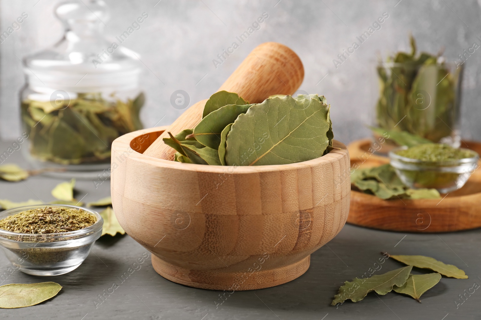 Photo of Wooden mortar with aromatic bay leaves and pestle on grey table