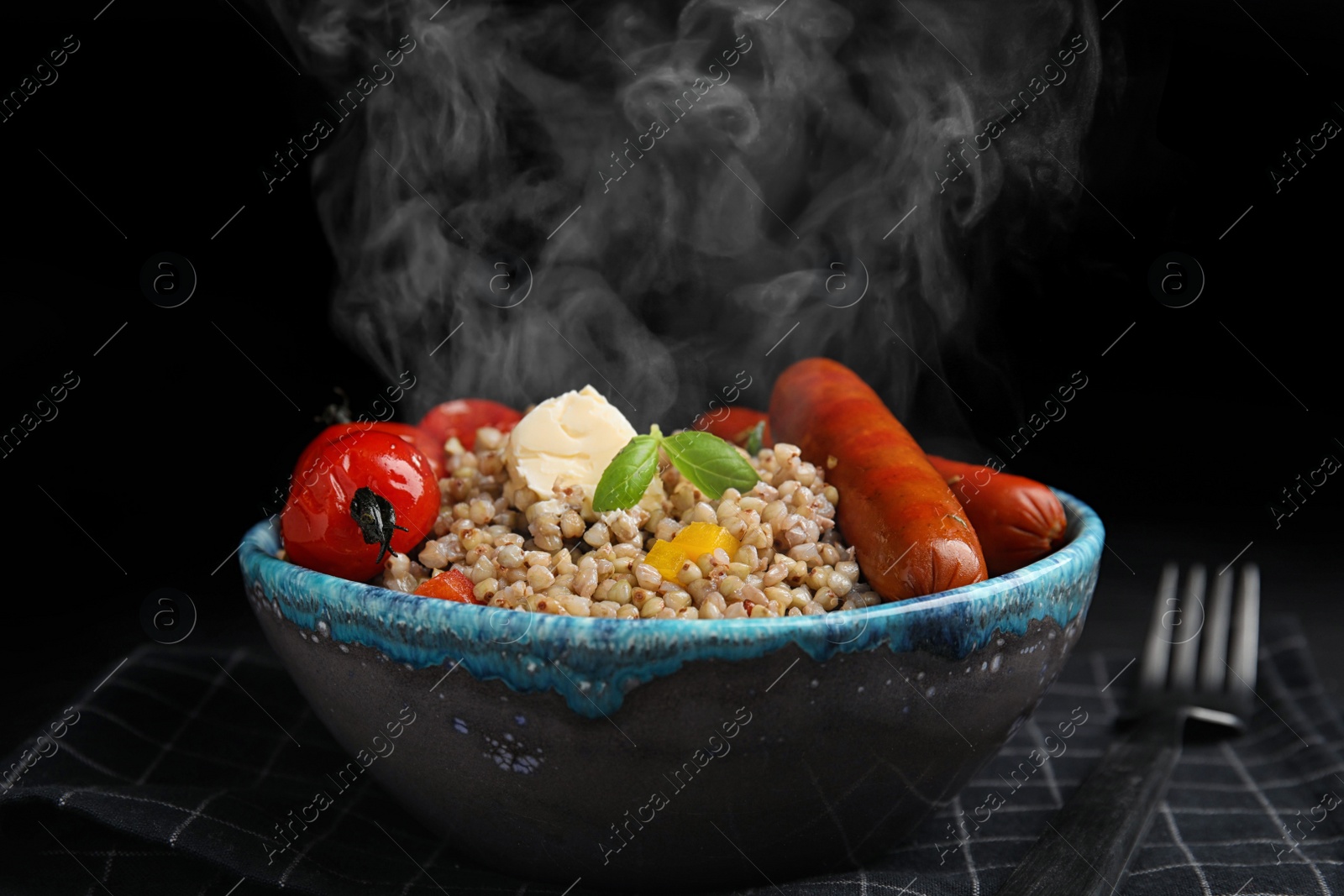 Image of Tasty buckwheat porridge with sausages on table against black background