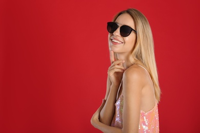 Photo of Beautiful woman in stylish sunglasses on red background. Space for text