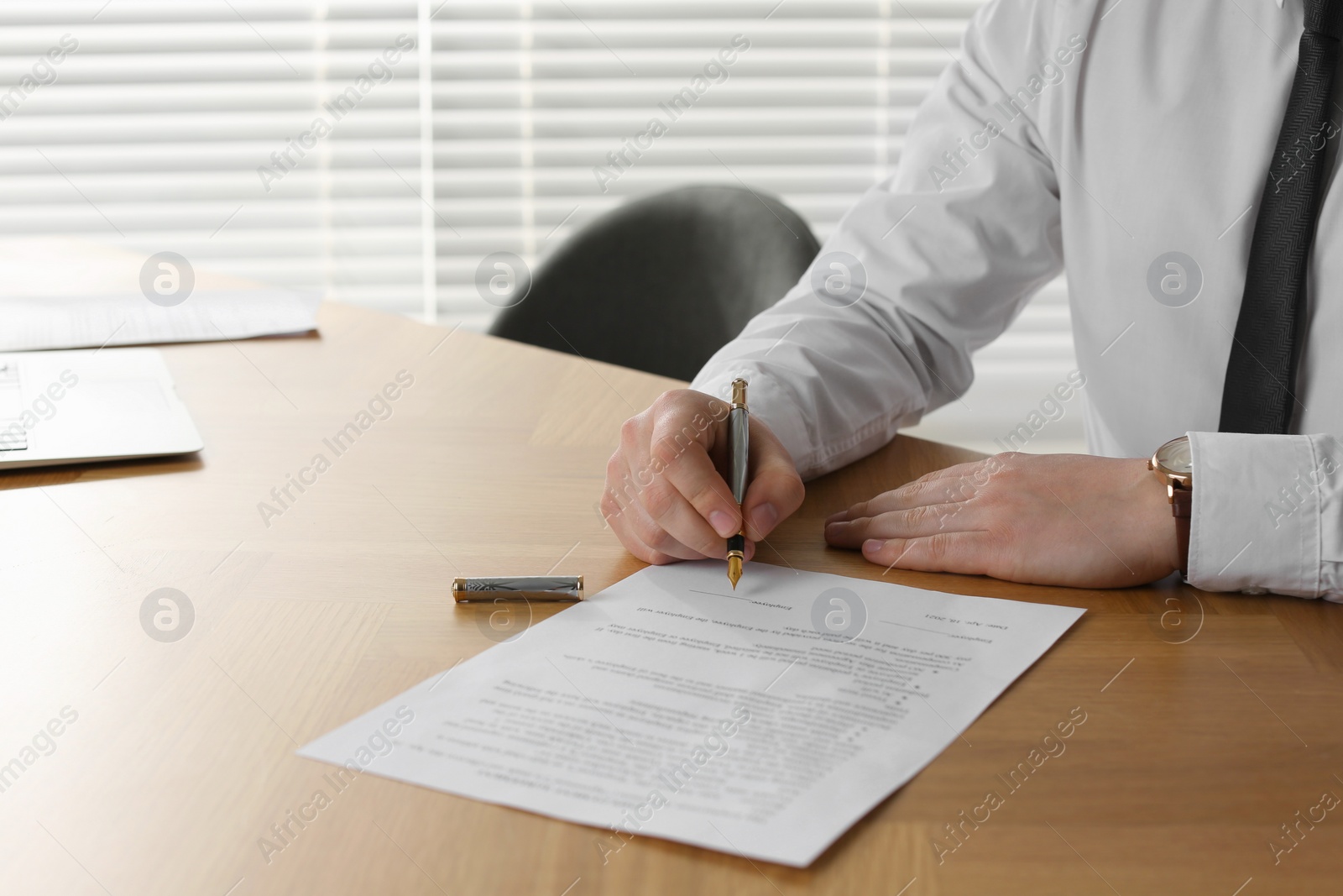 Photo of Notary signing document at wooden table in office, closeup