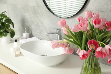 Vase with beautiful pink tulips and toiletries near sink in bathroom