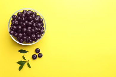 Photo of Fresh acai berries and green leaves on yellow background, flat lay. Space for text